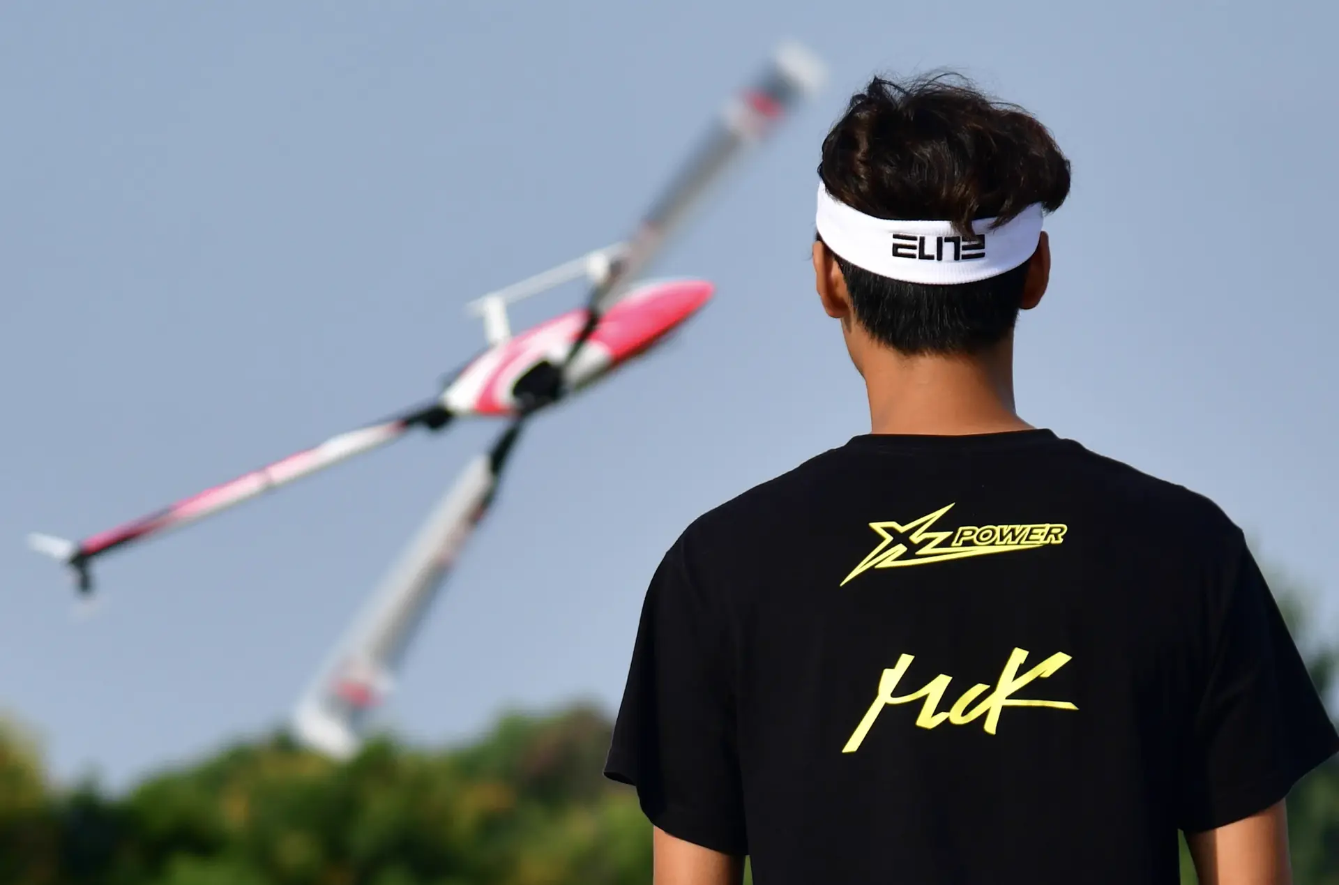 MinChan Kim flying his RC helicopter at a competition, MCK-branded shirt, viewed from behind